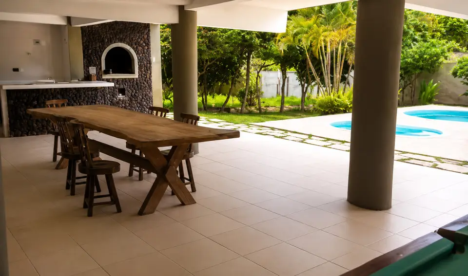 Área coberta de convivência com mesa de jantar, churrasqueira e vista para o jardim e piscina da clínica